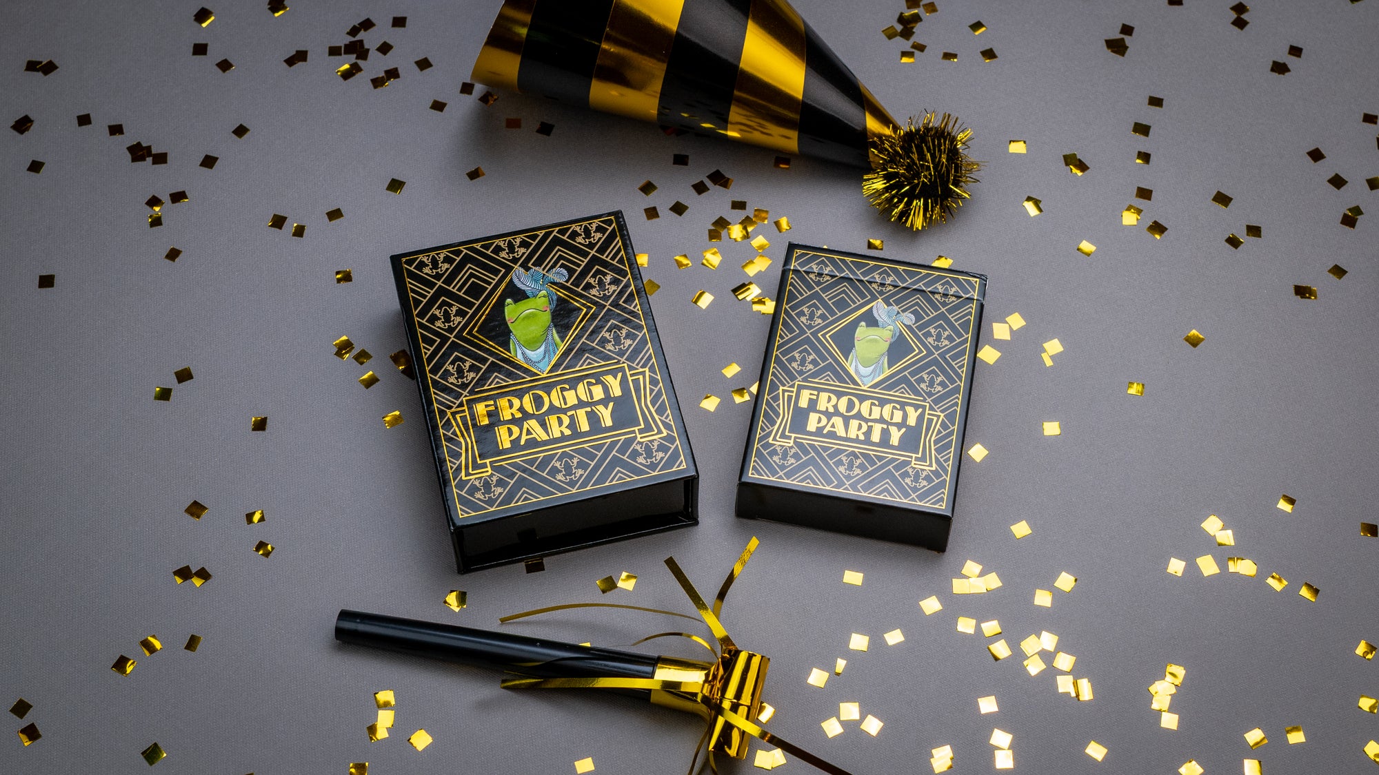 Two playing card boxes labeled 'Froggy Party' with confetti and a party hat on a gray background.