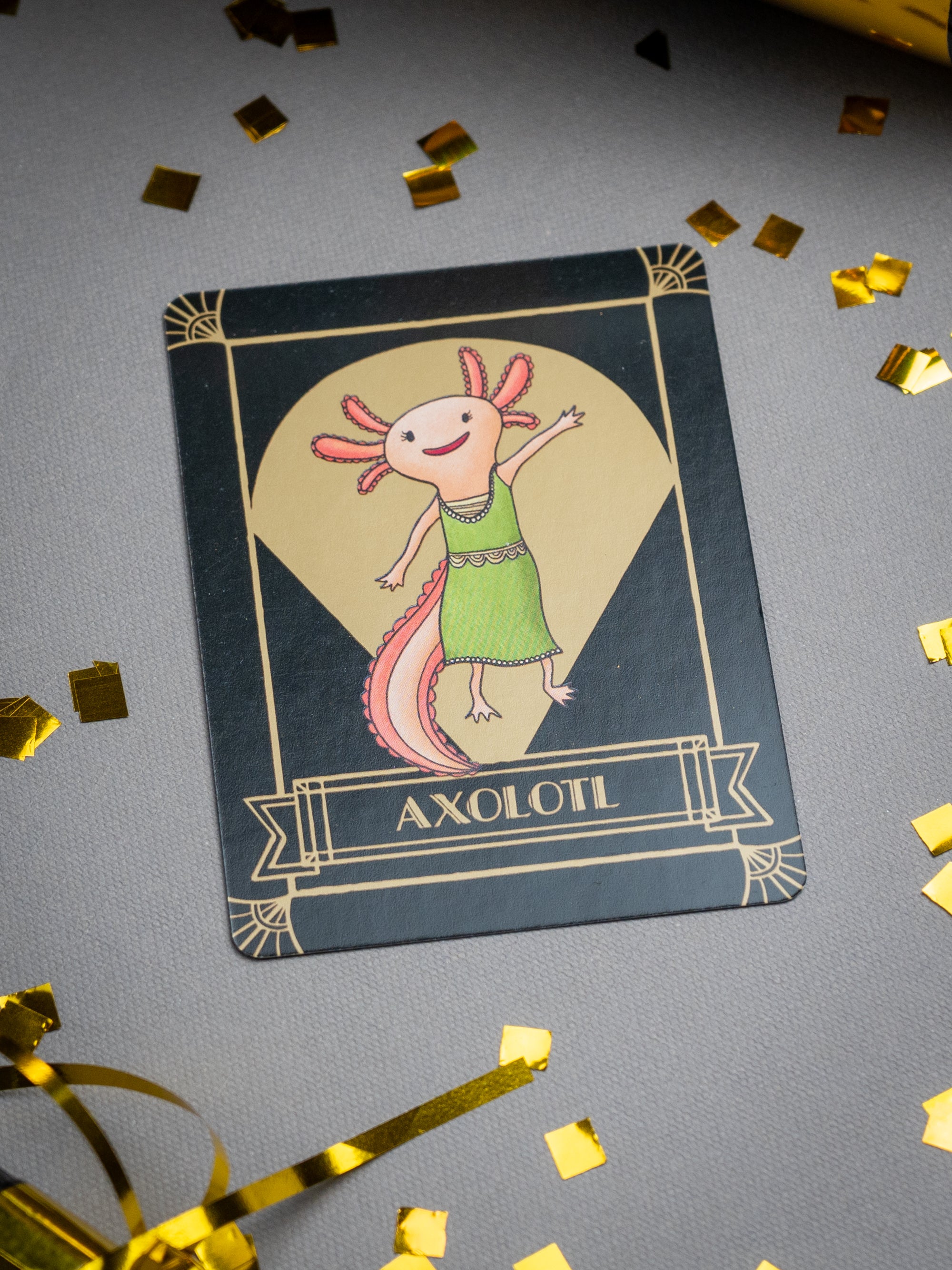 Card with an illustration of an axolotl set on a gray background with gold confetti.