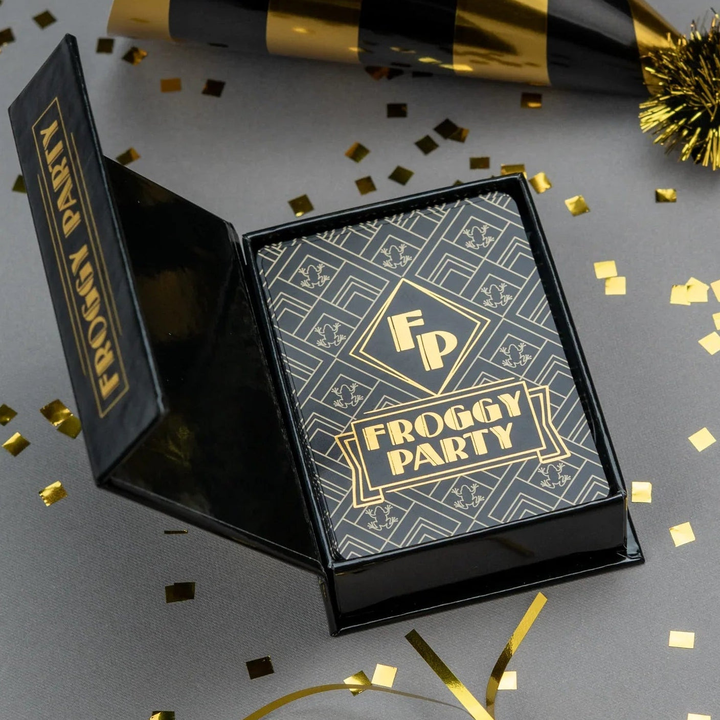 Froggy Party product packaging with black and gold colors on a gray background with confetti.