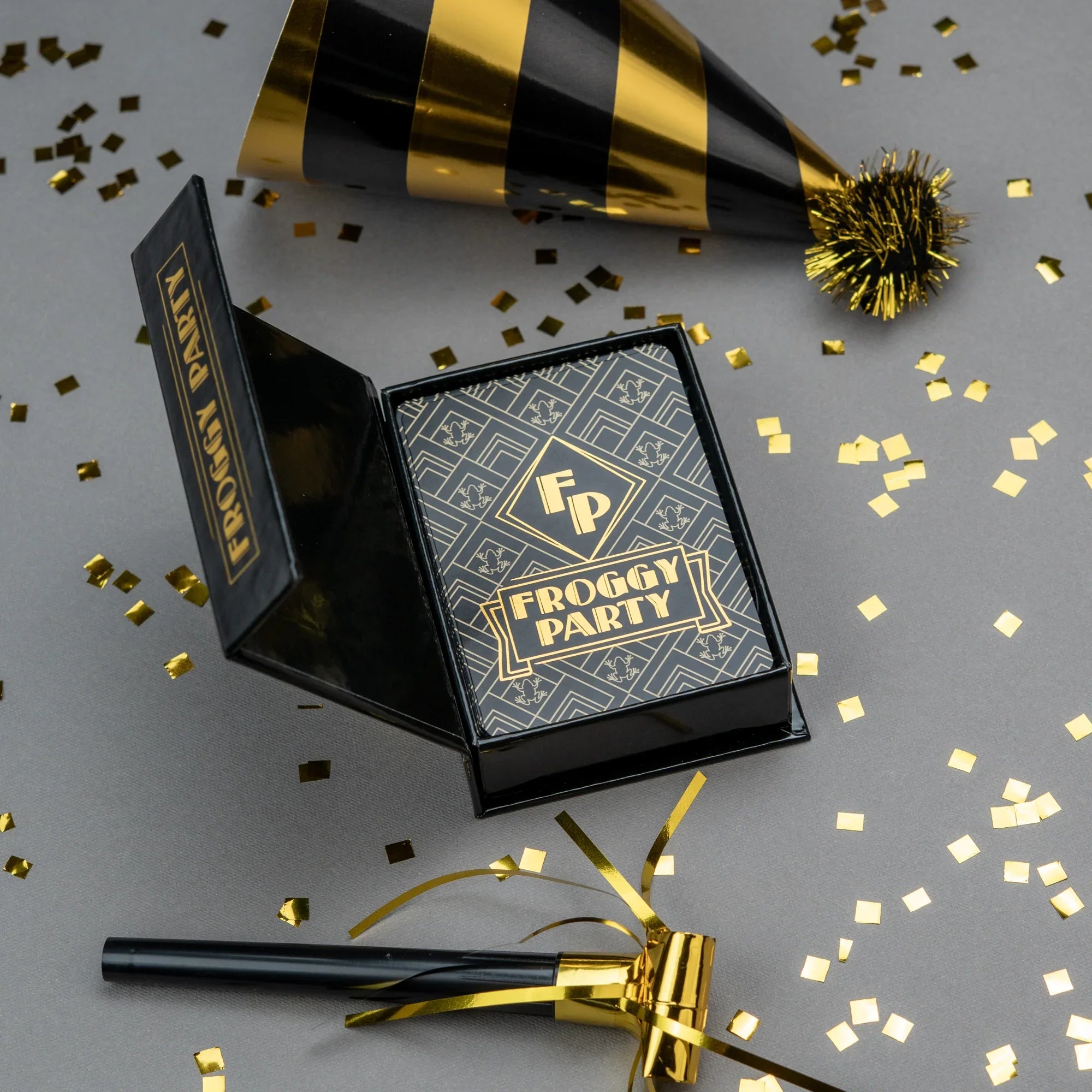 Froggy Party product packaging with black and gold colors on a gray background with confetti.